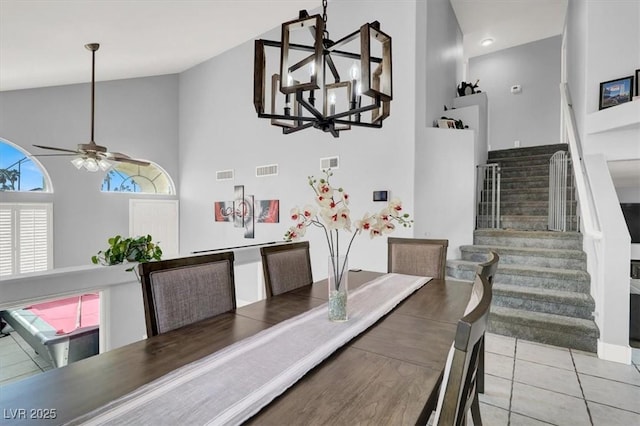 tiled dining space featuring high vaulted ceiling and ceiling fan with notable chandelier