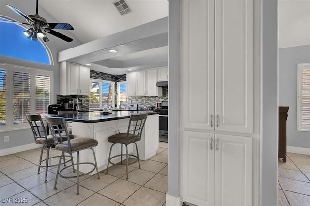 kitchen with a kitchen breakfast bar, vaulted ceiling, backsplash, white cabinets, and light tile patterned flooring