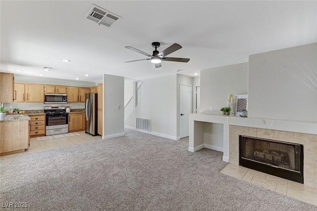 unfurnished living room with a tile fireplace, light carpet, and ceiling fan