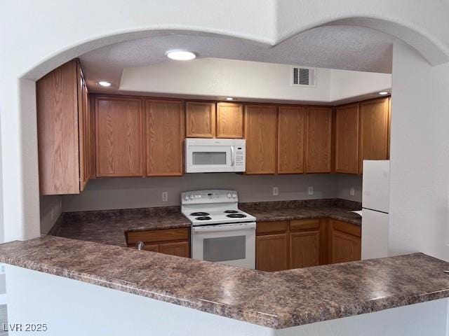 kitchen with white appliances, kitchen peninsula, and dark stone countertops