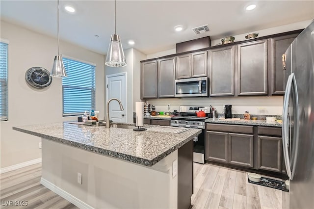 kitchen with appliances with stainless steel finishes, an island with sink, decorative light fixtures, and light stone counters