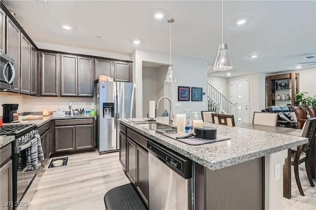 kitchen featuring pendant lighting, a center island with sink, appliances with stainless steel finishes, a kitchen breakfast bar, and sink