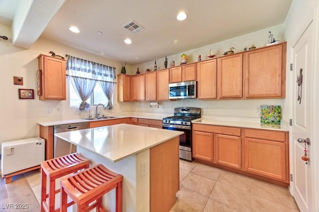 kitchen with sink, a center island, a kitchen bar, light tile patterned floors, and appliances with stainless steel finishes