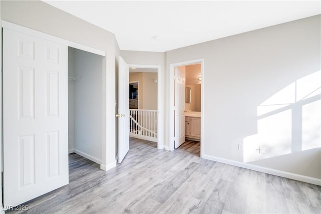 unfurnished bedroom featuring ensuite bath, a closet, and light hardwood / wood-style flooring