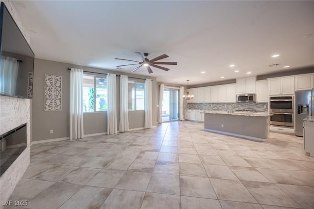 kitchen featuring hanging light fixtures, an island with sink, ceiling fan with notable chandelier, white cabinets, and appliances with stainless steel finishes