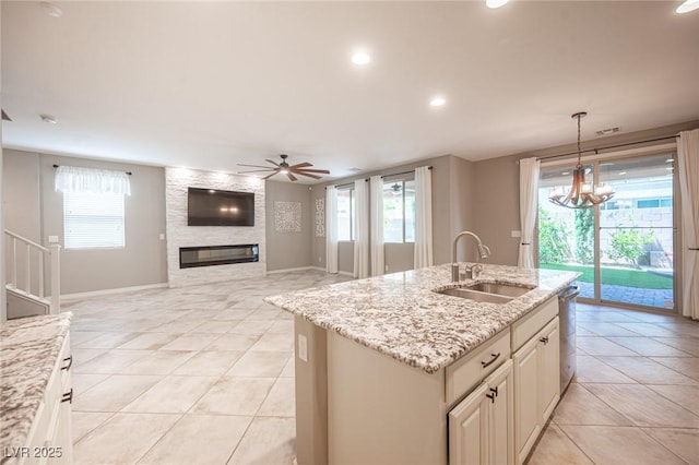 kitchen featuring a large fireplace, light stone countertops, pendant lighting, a center island with sink, and sink