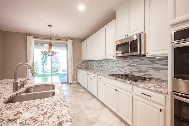 kitchen with stainless steel appliances, sink, white cabinetry, light stone countertops, and a notable chandelier