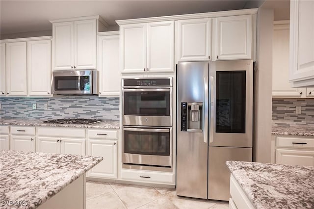 kitchen with white cabinets, stainless steel appliances, light stone countertops, and tasteful backsplash