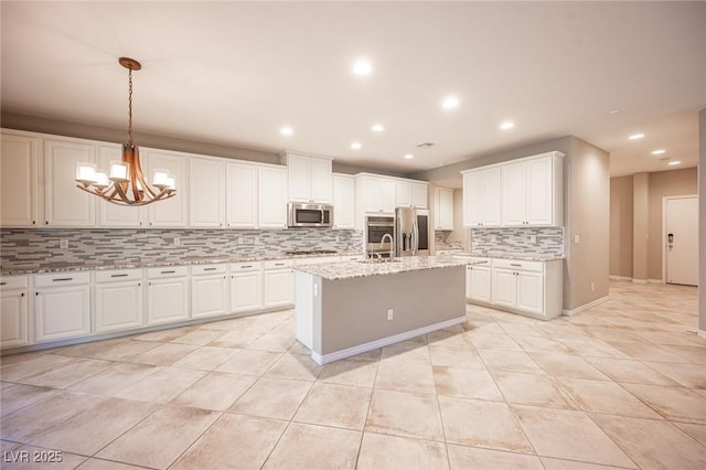 kitchen with light stone counters, decorative light fixtures, stainless steel appliances, an island with sink, and white cabinetry