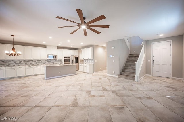 kitchen featuring pendant lighting, stainless steel appliances, a kitchen island, ceiling fan with notable chandelier, and white cabinets