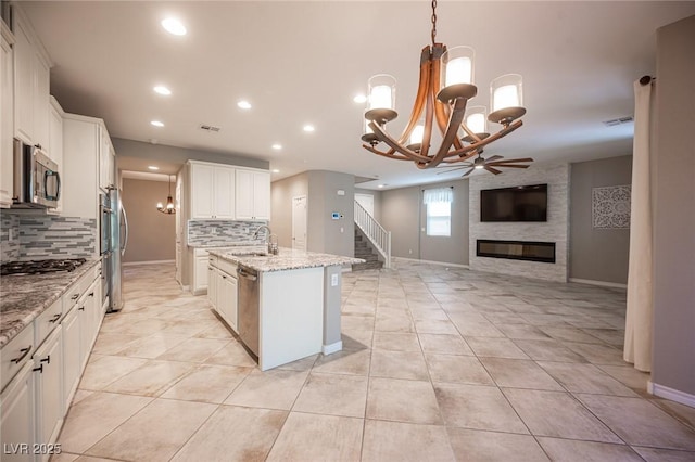 kitchen featuring stainless steel appliances, white cabinets, a kitchen island with sink, and tasteful backsplash