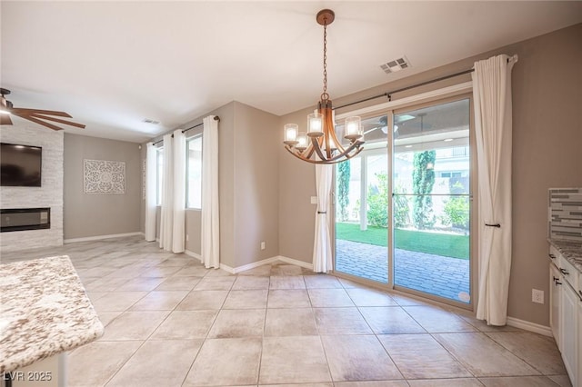 unfurnished dining area with ceiling fan with notable chandelier, a fireplace, and light tile patterned flooring