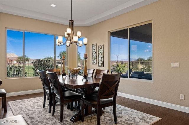 dining area with a raised ceiling, an inviting chandelier, and dark hardwood / wood-style floors