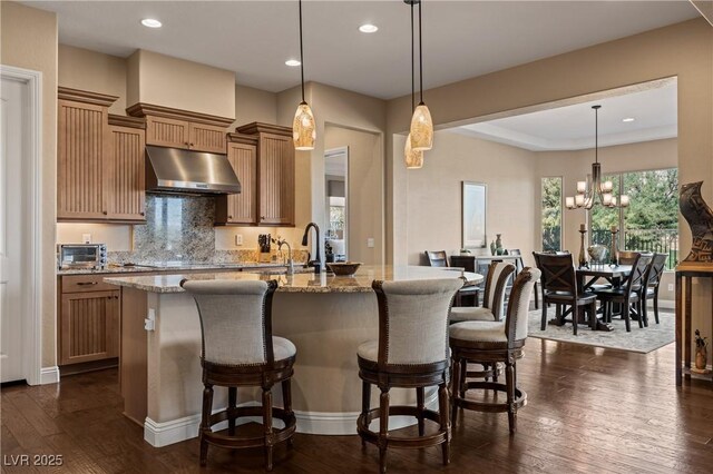 kitchen with hanging light fixtures, an inviting chandelier, range hood, and light stone countertops