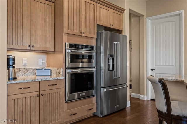 kitchen with stainless steel appliances, light stone counters, dark wood-type flooring, and light brown cabinets