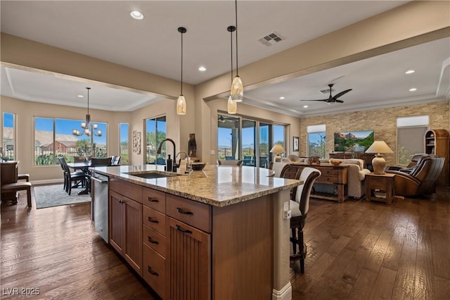 kitchen with light stone countertops, pendant lighting, a center island with sink, ceiling fan with notable chandelier, and sink