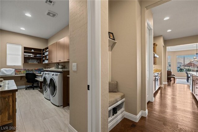 clothes washing area featuring washing machine and clothes dryer, a chandelier, light hardwood / wood-style floors, and cabinets