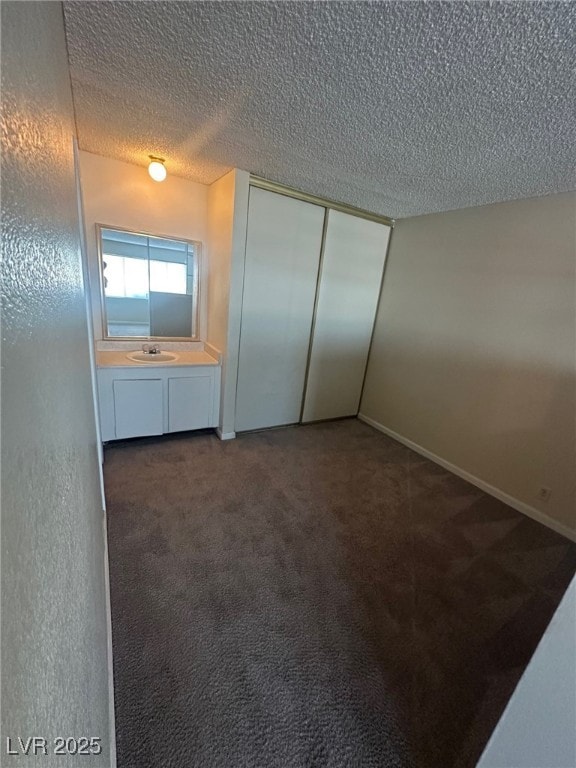 unfurnished bedroom with a textured ceiling, a closet, sink, and dark colored carpet