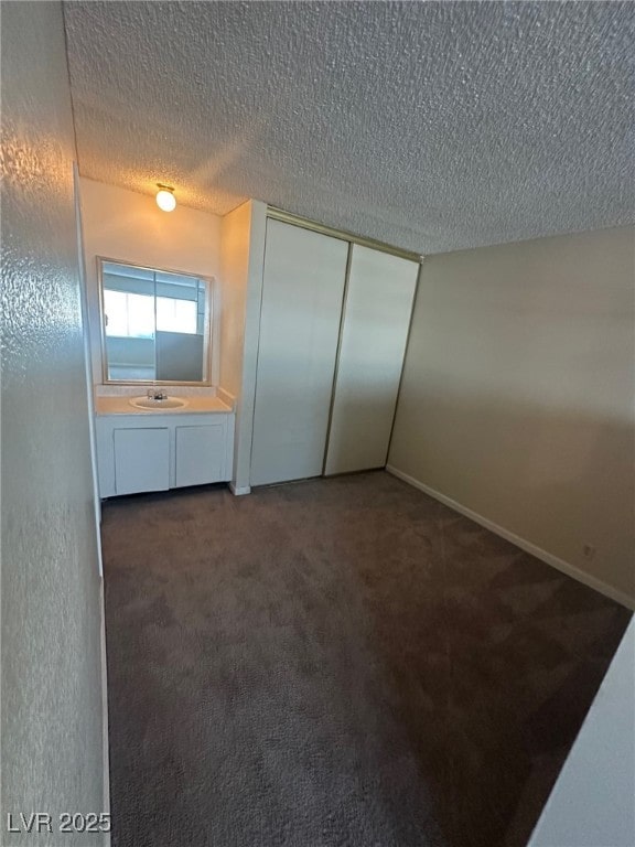 unfurnished bedroom featuring a textured ceiling, a closet, dark carpet, and sink