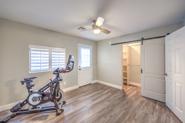 workout area with ceiling fan, a barn door, and light hardwood / wood-style flooring