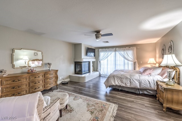 bedroom featuring a multi sided fireplace, a textured ceiling, ceiling fan, and dark hardwood / wood-style floors