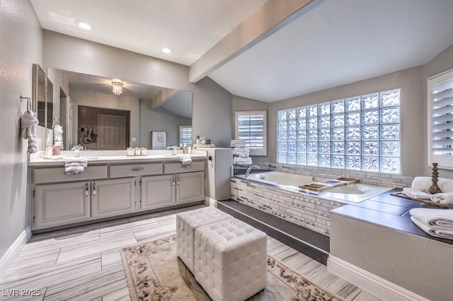 bathroom featuring vanity, lofted ceiling with beams, and tiled bath