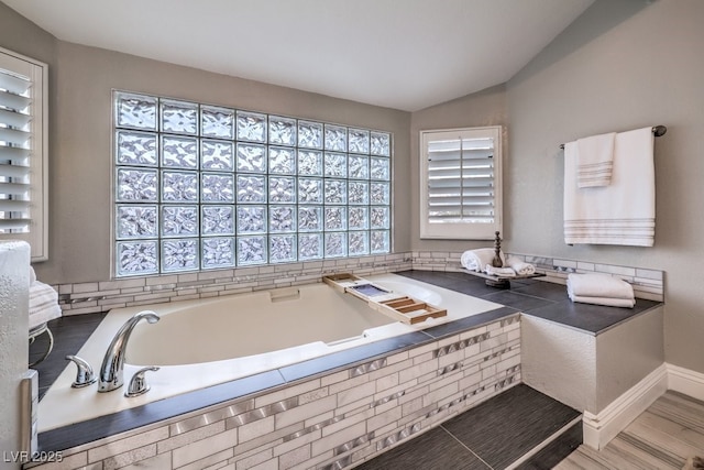 bathroom featuring a relaxing tiled tub and lofted ceiling