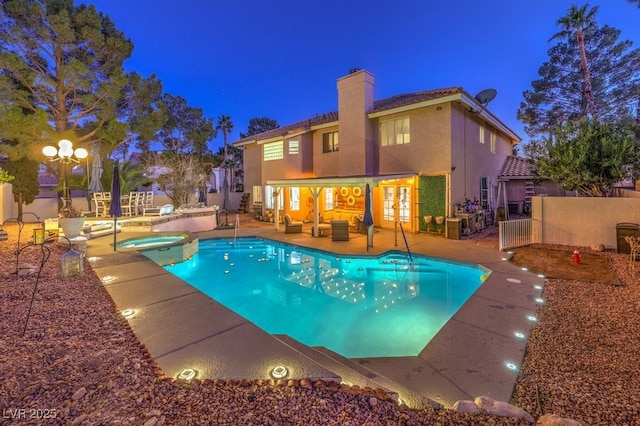 pool at night with outdoor lounge area, an in ground hot tub, and a patio area