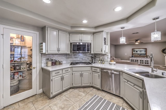 kitchen with sink, ceiling fan, a tray ceiling, pendant lighting, and appliances with stainless steel finishes