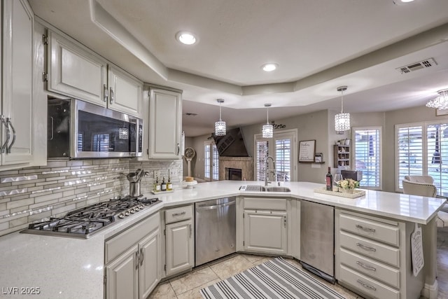 kitchen featuring appliances with stainless steel finishes, kitchen peninsula, a tray ceiling, sink, and tasteful backsplash