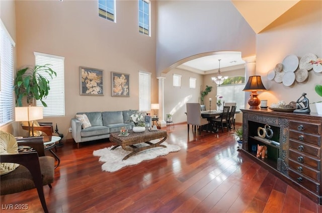 living room with a towering ceiling, dark wood-type flooring, decorative columns, and a chandelier