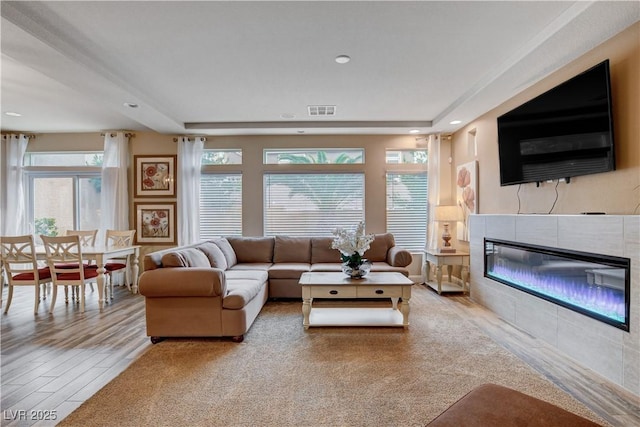 living room featuring a tiled fireplace, plenty of natural light, and light hardwood / wood-style flooring