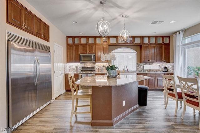 kitchen with decorative light fixtures, light stone counters, a kitchen island, a chandelier, and appliances with stainless steel finishes