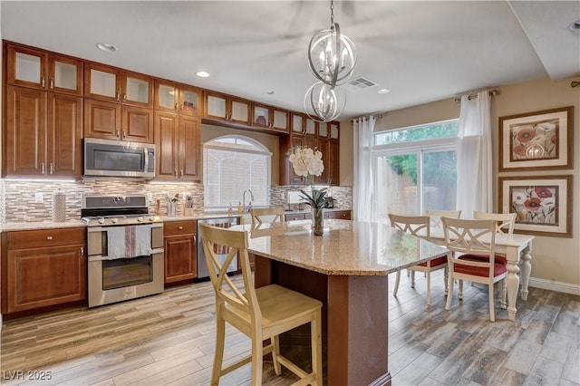 kitchen with a chandelier, a center island with sink, appliances with stainless steel finishes, decorative backsplash, and decorative light fixtures