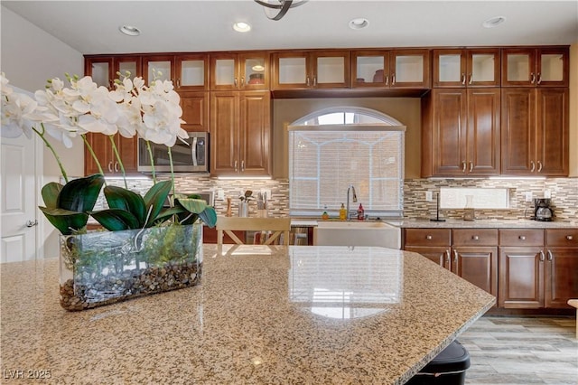 kitchen with light stone counters, light hardwood / wood-style floors, tasteful backsplash, and sink