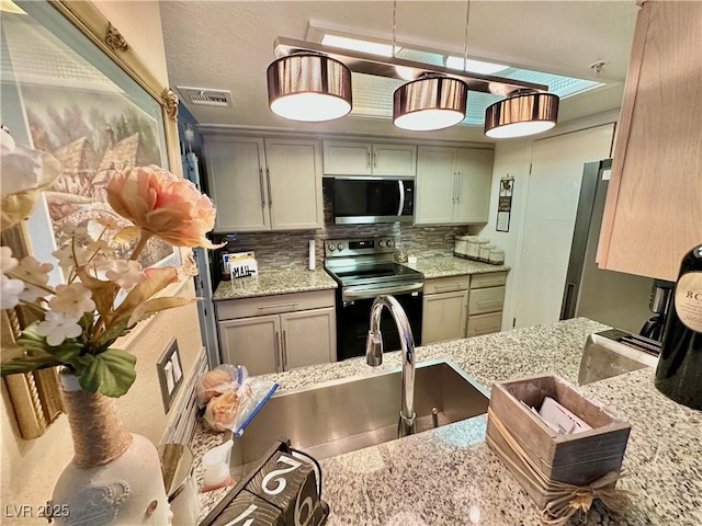 kitchen with appliances with stainless steel finishes, sink, backsplash, and light stone countertops