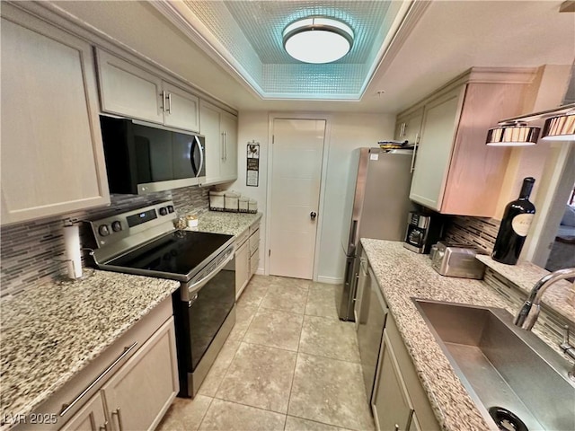 kitchen featuring stainless steel appliances, decorative backsplash, a tray ceiling, sink, and light tile patterned flooring