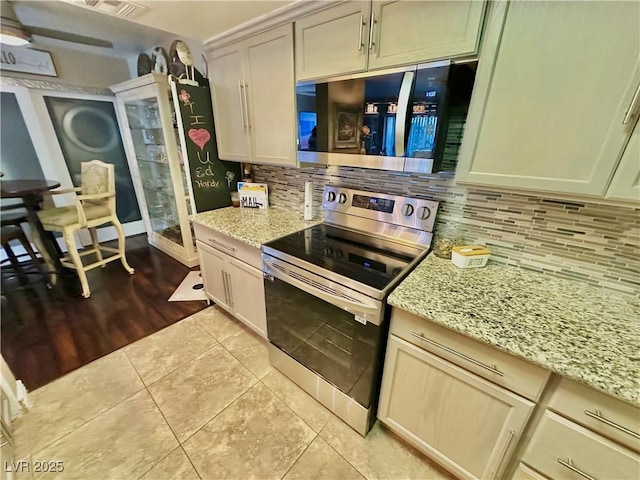 kitchen featuring light stone counters, stainless steel appliances, light tile patterned floors, and decorative backsplash