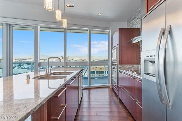 kitchen featuring appliances with stainless steel finishes, a water view, light stone counters, sink, and decorative light fixtures