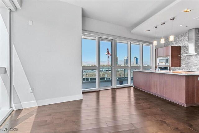 kitchen featuring hanging light fixtures, a wealth of natural light, wall chimney exhaust hood, and stainless steel microwave