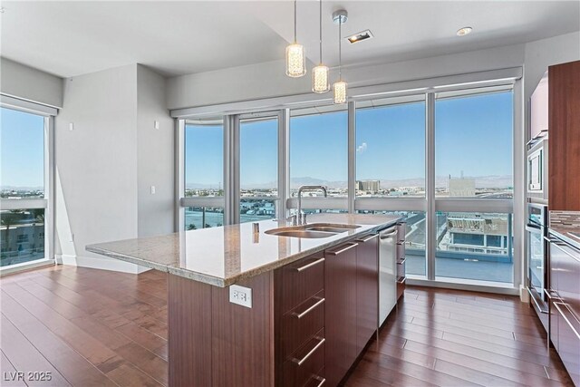 kitchen featuring sink, dark hardwood / wood-style flooring, decorative light fixtures, and an island with sink