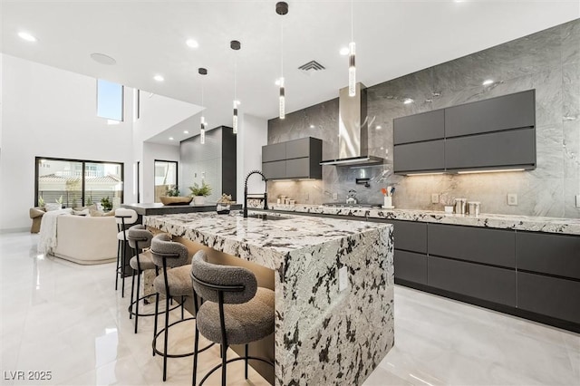 kitchen with hanging light fixtures, a breakfast bar, a spacious island, sink, and wall chimney range hood