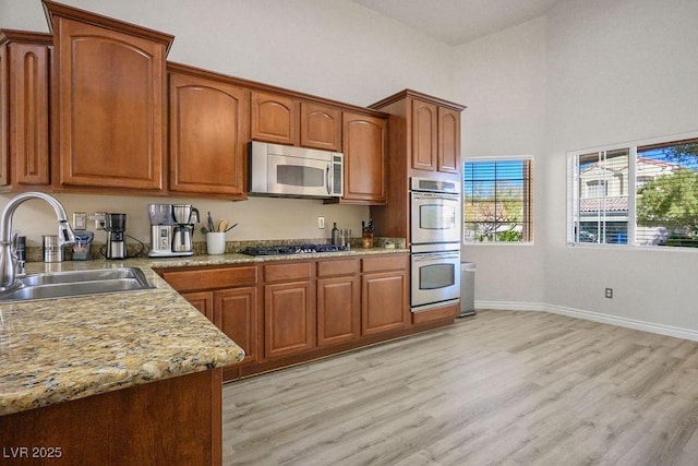 kitchen featuring light stone countertops, appliances with stainless steel finishes, light hardwood / wood-style floors, and sink