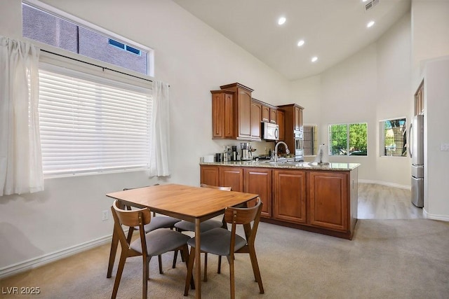 kitchen featuring stainless steel appliances, light colored carpet, kitchen peninsula, high vaulted ceiling, and sink