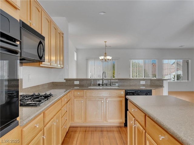 kitchen featuring black appliances, hanging light fixtures, a notable chandelier, light brown cabinetry, and sink