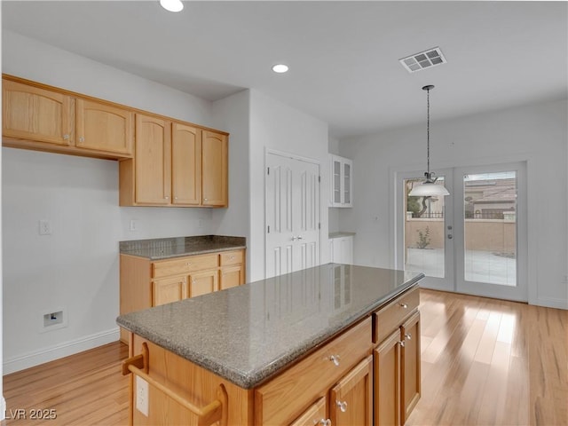 kitchen with dark stone counters, light wood-type flooring, decorative light fixtures, and a kitchen island