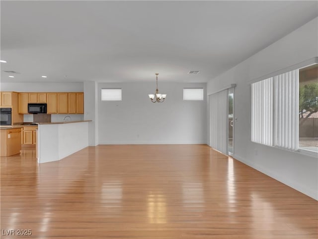 unfurnished living room featuring light hardwood / wood-style floors, a healthy amount of sunlight, and a notable chandelier