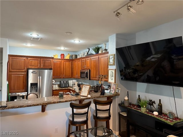 kitchen featuring a breakfast bar, kitchen peninsula, stainless steel appliances, and dark stone counters