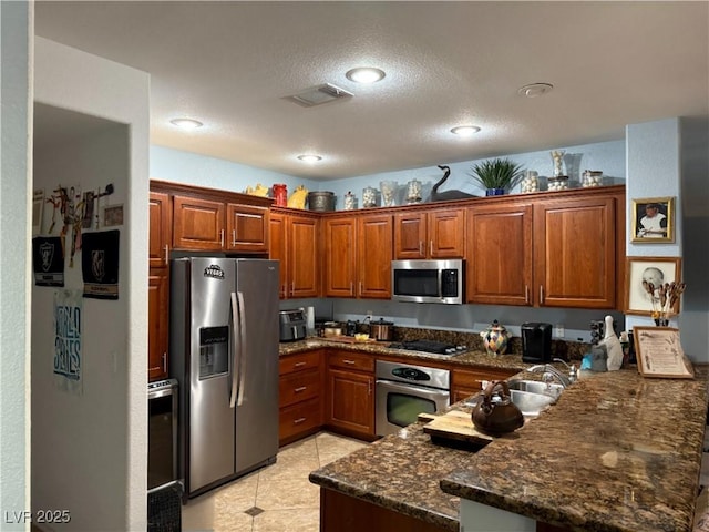 kitchen with light tile patterned floors, kitchen peninsula, stainless steel appliances, dark stone counters, and sink