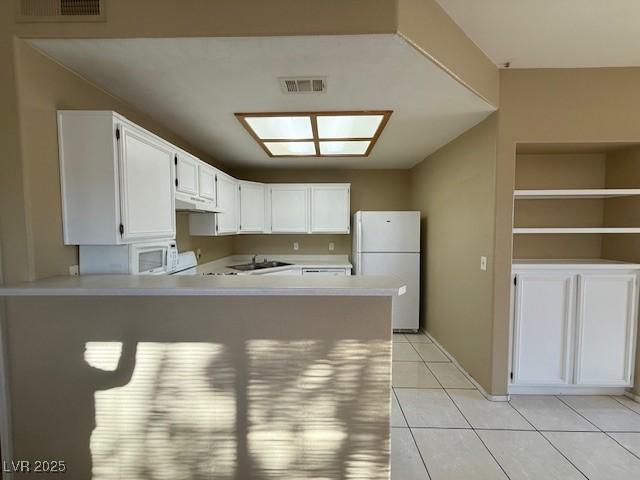 kitchen featuring white appliances, kitchen peninsula, white cabinets, light tile patterned flooring, and sink